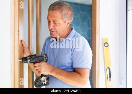 Professional middle-aged repairman screwing the door with a screwdriver during installation indoors Stock Photo