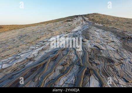 Cracked surface of a mud volcano in Berca, Romania, with dried mud flow patterns under a clear sky at sunset in a barren desert-like environment Stock Photo