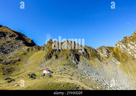 Mountain refuge in Balea, Transfăgărășan, Romania, with red roof nestled at the base of rugged rocky peaks under a clear blue sky Stock Photo