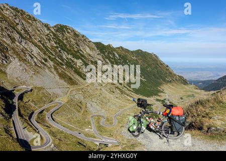 Loaded touring bicycle overlooking the Transfăgărășan winding mountain road in a remote alpine landscape under a clear blue sky Stock Photo