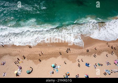 Overhead drone shot of anonymous tourist and colorful parasols on sandy seashore. From above of people enjoying summer vacations at beach during sunny day Stock Photo