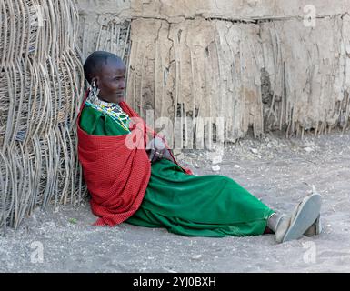 Elderly Maasai woman sitting on dirt floor outside her hut Tanzania,  East Africa Stock Photo