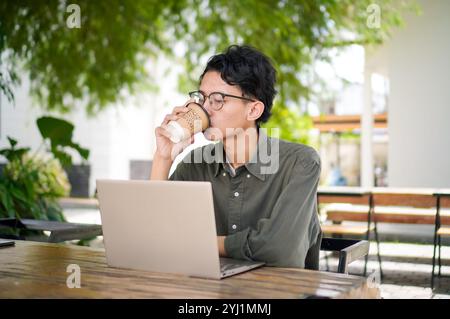Asian man working on laptop at the outdoor cafe. A man working on laptop while drinking a cup of coffee. Stock Photo