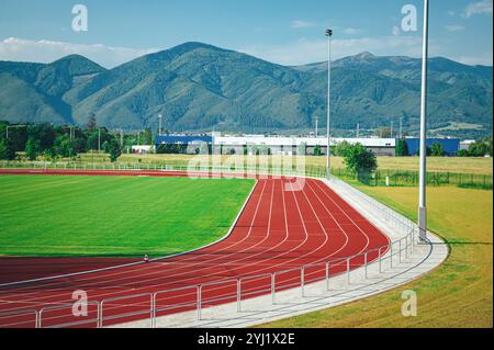 Aerial View of a Modern Athletic Stadium Surrounded by Green Meadows with an 8-Lane Red Tartan Track, Capturing the Beauty of Sports Architecture in a Stock Photo