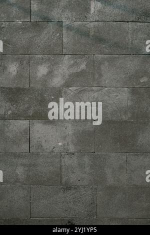A close-up view of a stone wall with rectangular, textured grey tiles. Subtle patterns and weathered marks add character to the surface, creating a ra Stock Photo