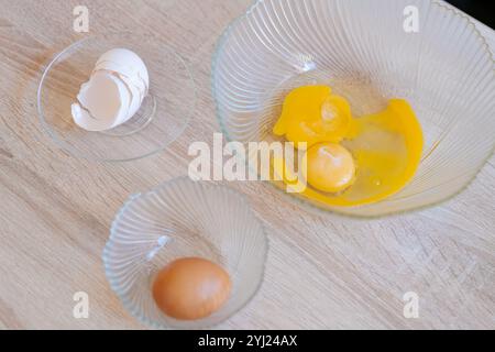 Bowl of eggs sits on a table next to two other bowls. One bowl has a piece of eggshell in it Stock Photo