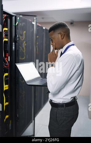 Man, technician or thinking with laptop screen in server room for software, hardware or network repair. Male person, IT engineer or wonder with Stock Photo