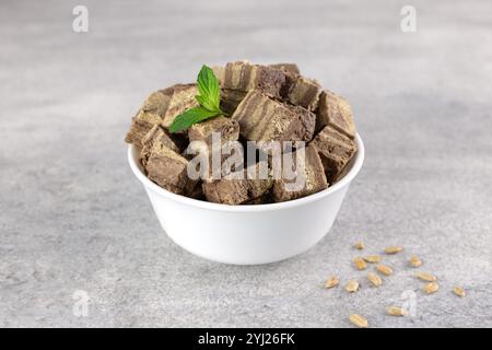 Pieces of halva with cocoa in white plate on gray background. Sweet Turkish, Iranian dessert with mint leaves. Stock Photo