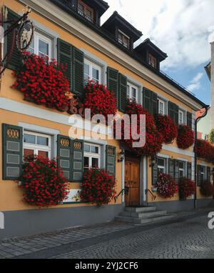 Yellow building with lots of red flowers in window planters. Street in the old town. Stock Photo