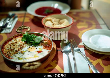 A table set for a meal with dishes of soup, fresh herbs, plates and utensils on a patterned tablecloth, Portugal Stock Photo