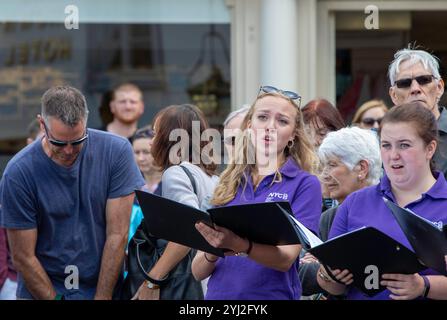 Late summer in Framlingham Suffolk the National Youth Choir of Great Britain in matching purple polo shirts perform an outdoor concert on the Market Stock Photo