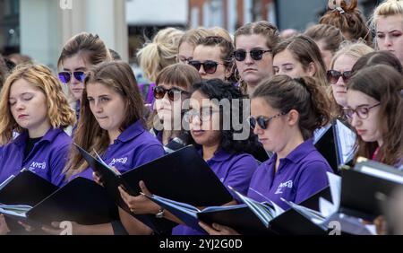 Late summer in Framlingham Suffolk the National Youth Choir of Great Britain in matching purple polo shirts perform an outdoor concert on the Market Stock Photo