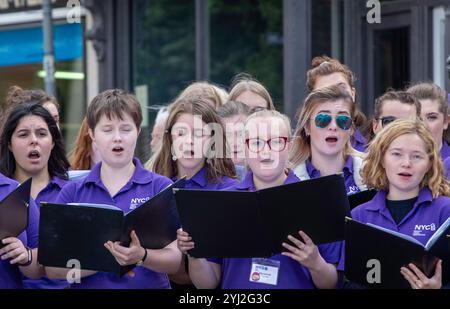 Late summer in Framlingham Suffolk the National Youth Choir of Great Britain in matching purple polo shirts perform an outdoor concert on the Market Stock Photo