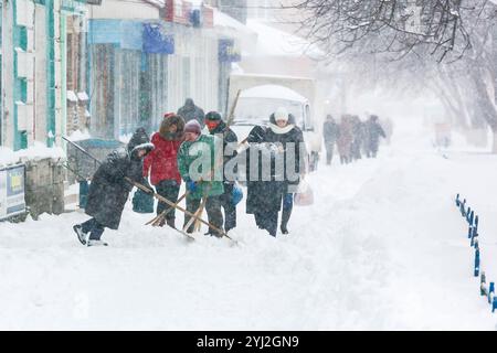 Ukraine, city of Romny, 01.08.2016: A snowy city street during a heavy snowfall. People with snow shovels clear sidewalks in winter during snowfall. W Stock Photo