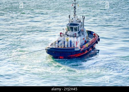 Red and blue tugboat towing a large unseen vessel on the open sea, Singapore Stock Photo