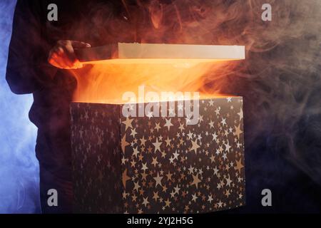 human hands taking out surprise from mysterious box on dark red background surrounded by smoke, mystery box Stock Photo