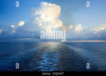 Cumulus clouds tower over the ocean at sunset with a ship's wake leading towards the horizon, South China Sea Stock Photo