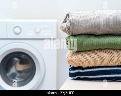 A stack of neatly folded clothes on a table with a washing machine in the background. Stock Photo