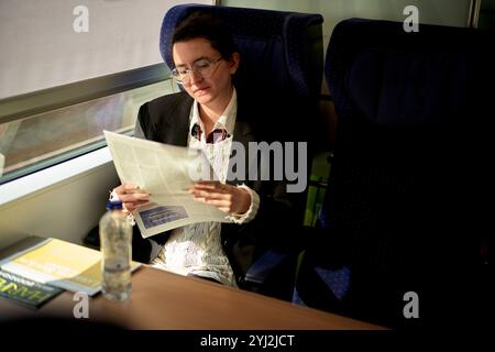 Woman reading a newspaper while traveling in a train with a bottle of water on the table Stock Photo