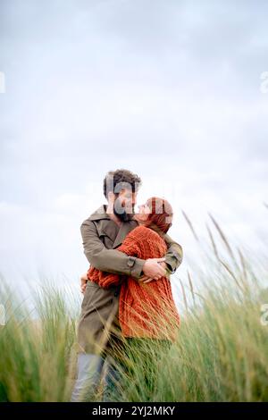 Couple embracing and kissing in a grassy field under an overcast sky, Belgium Stock Photo