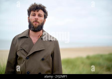 Bearded man in a trench coat standing at the beach with dunes in the background, Belgium Stock Photo