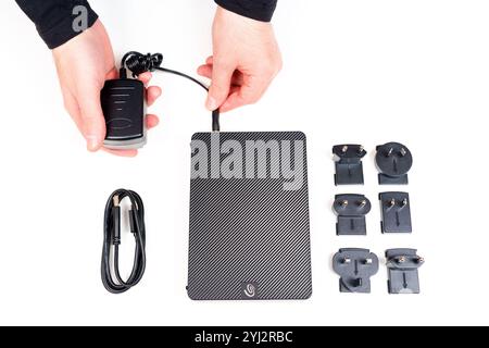 Kyiv, Ukraine - October 23, 2024: Hands connecting the power adapter to the Seagate Expansion external hard drive with various plug types arranged on Stock Photo