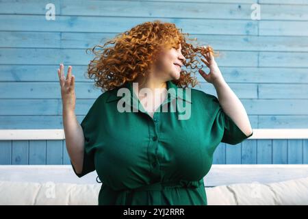 Beautiful Happy Plus Size Woman Enjoying Life, Dancing and Shaking Hair with Joy, Confidence and Positive Emotions Outdoors Against Blue Background Stock Photo