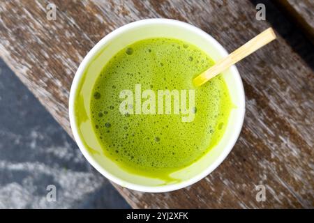 Organic matcha latte in a recyclable paper cup with a frothy texture, placed on a rustic wooden surface. Vibrant green drink promoting sustainable hea Stock Photo
