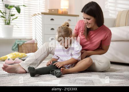 Mother helping her daughter to put tights on at home Stock Photo