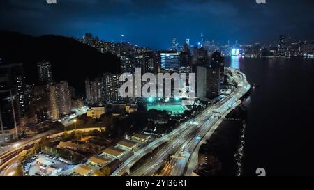 A stunning view captures the illuminated buildings and bustling life of Hong Kong at night along the harbor. Stock Photo