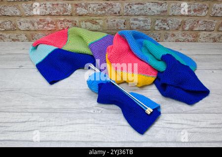 Looking down on a light blue ball of wool with knitting needles and a knitted patchwork blanket behind Stock Photo