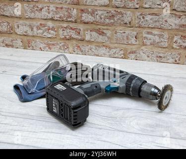 Rechargeable drill fitted with a rotary wire brush placed on a worktop along with work gloves eye proaction glasses Stock Photo