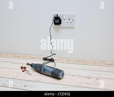 Rechargeable mini rotary tool fitted with a sanding drum placed on the floor connected to a charger Stock Photo