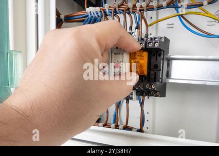 Close up of a hand inserting an electrical relay into a control panel with visible wiring and components. Stock Photo