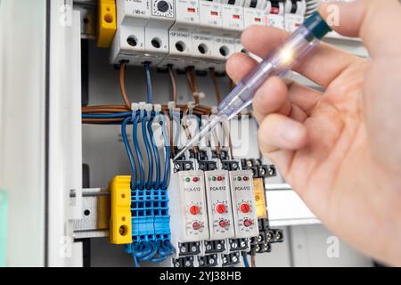 Electrician Testing Electrical Connections with Voltage Tester in Control Panel Stock Photo