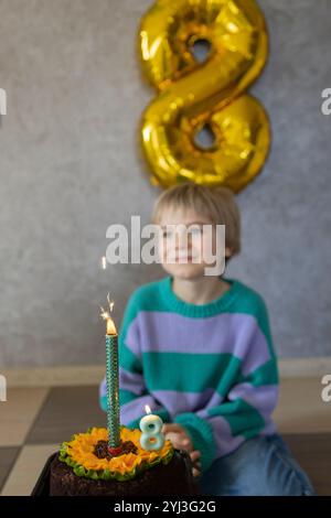 cute dreamy birthday boy looks at the cake and burning candles, number 8. birthday party. Holiday, congratulations, happiness, joy, pleasure Stock Photo