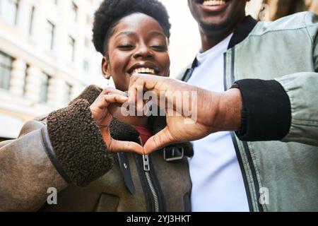 Smiling Couple Making Heart Shape with Hands Outdoors in Urban Setting, Expressing Love and Happiness Stock Photo