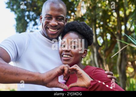 Cheerful Couple Making Heart Gesture in Sunny City Park Stock Photo