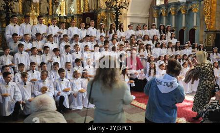 Grodno, Belarus - May 15, 2023: Large group of children celebrating first holy communion in a catholic church, parents taking photos Stock Photo