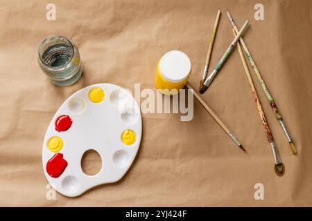 Art supplies arranged on table with paint palette, brushes, and water jar, at home Stock Photo