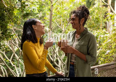 Friends enjoying coffee and laughter on balcony surrounded by nature Stock Photo