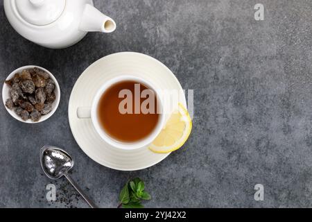 Teapot, cup of black tea in white ceramic mug with lemon and sugar on gray background. Top view. Copy Space. Stock Photo