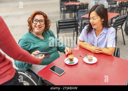 Woman with disability and asian friend paying with credit card in a sidewalk cafeteria Stock Photo