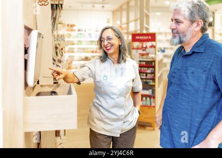 Female pharmacist using computer to give explanation to a mature male client pointing the screen and talking Stock Photo