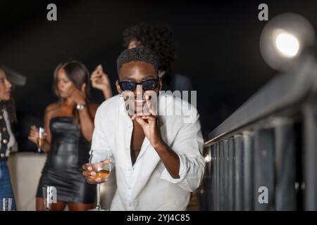 Latin cool man gesturing while dancing and drinking alcohol during roof party at night Stock Photo
