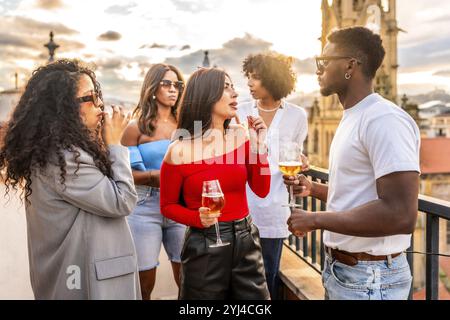 Multi-ethnic people celebrating evening party on rooftop drinking wine and chatting Stock Photo