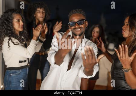 Brunette cool man in sunglasses gesturing while dancing surrounded by friends at night in a city roof Stock Photo