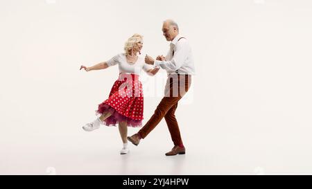 Dynamic image of elderly couple performing lindy hop dance classic moves, dressed in retro clothing, isolated on white background Stock Photo