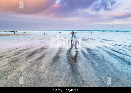 Pastel coloured sky over low tide as a man is walking on Gt Western Beach on the coast of Newquay in Cornwall in the UK. Stock Photo