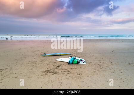 Pastel coloured sky over low tide with surfboards and bags left on Gt Western Beach on the coast of Newquay in Cornwall in the UK. Stock Photo